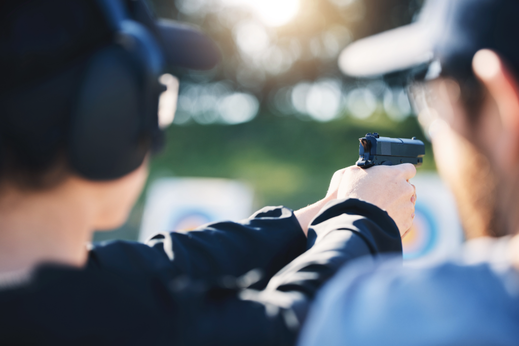 Man wearing protective headgear holding a gun with an instructor beside him.